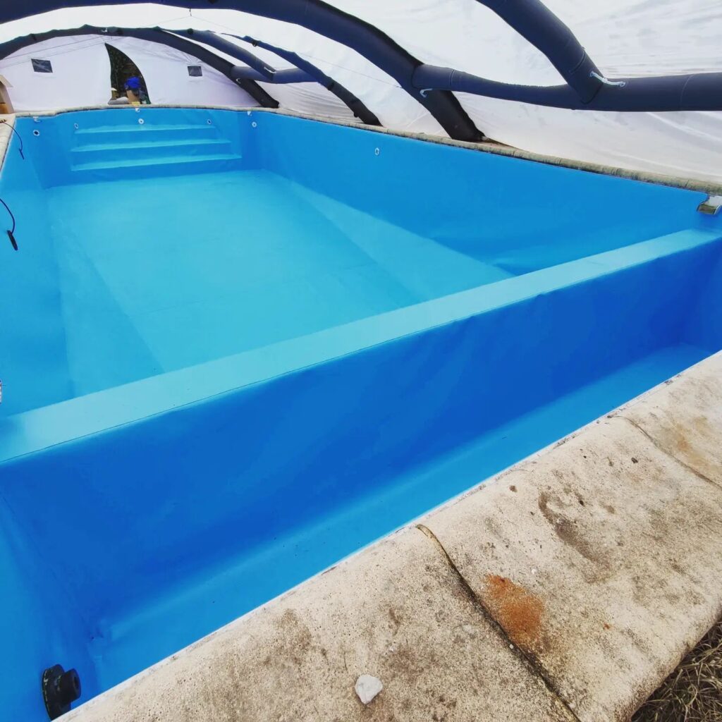 Liner Piscine Bleu : Installation Sous Abri Gonflable Piscine rectangulaire vide avec liner bleu vif sous un abri gonflable blanc et noir. Margelles en béton clair salies.